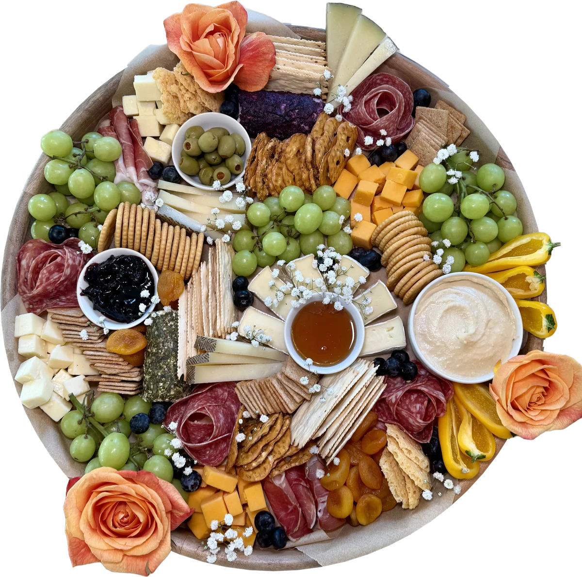 Round charcuterie board with peach roses, salami roses, cheeses, green grapes, olives, honey, hummus and mini peppers