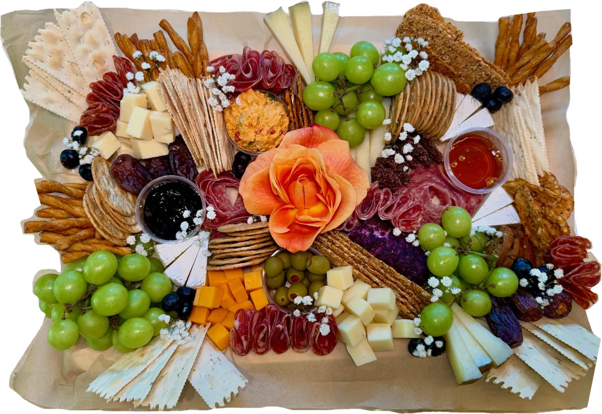 Rectangular charcuterie board with a peach rose, salami, cheeses, green grapes, crackers, breadsticks, honey and jam